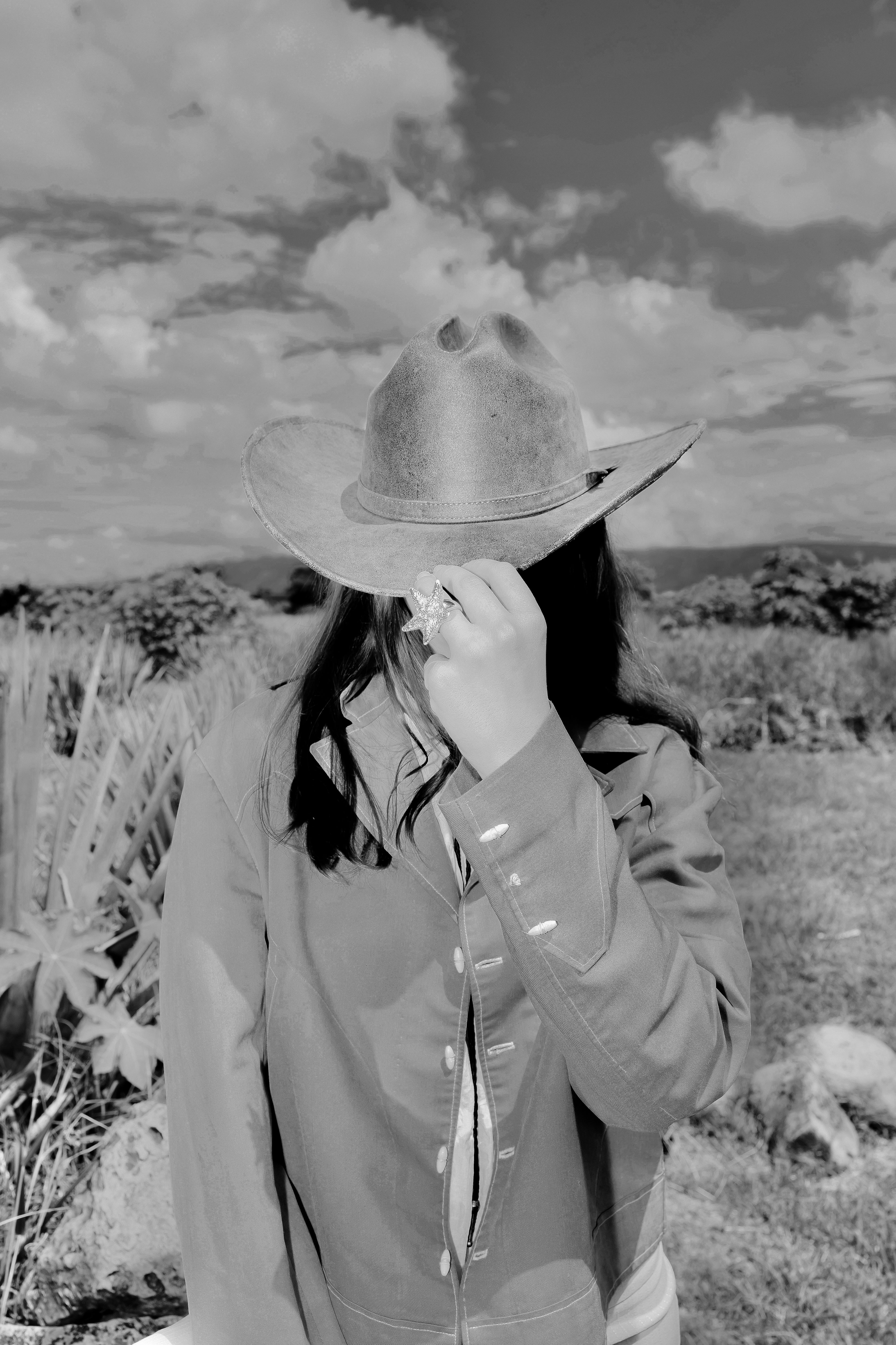 Person wearing a wide-brimmed hat in a field with a cloudy sky.